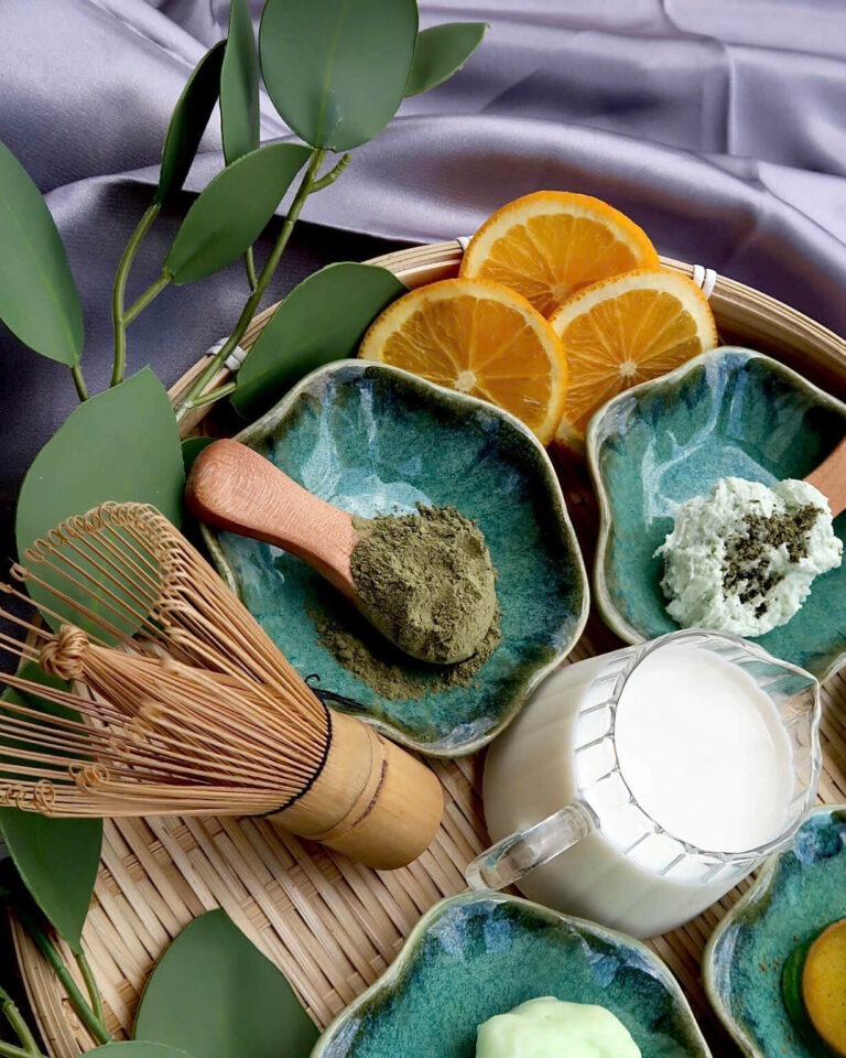 Green bowls with powders, creams, orange slices and a bamboo whisk